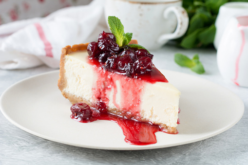Slice of new york cheesecake with cherry sauce and mint leaf on top.