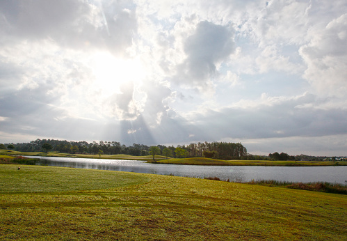 sun peeking through the clouds at early morning on a florida golf course beside a pond