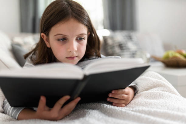 istock Cute young girl reading book at home 823962370