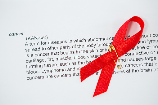 High angle view of red AIDS Awareness ribbon on paper with cancer text