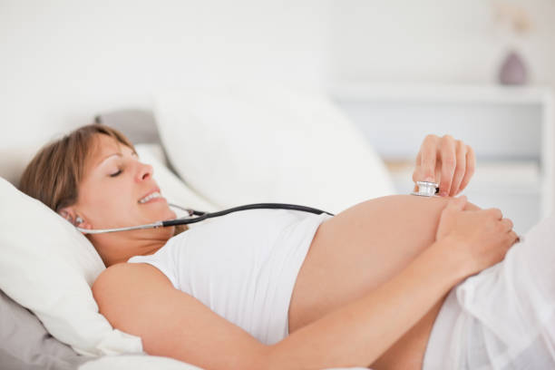 istock Cute pregnant woman using a stethoscope while lying on a bed 823978654