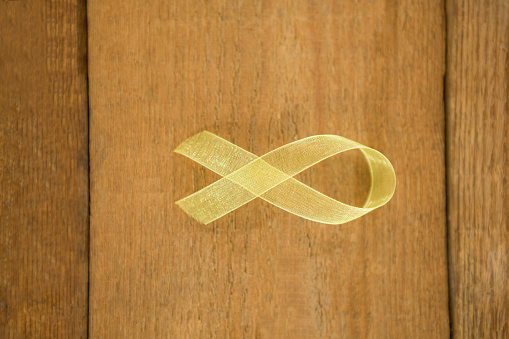 Directly above view of yellow Sarcoma Awareness ribbon on wooden table