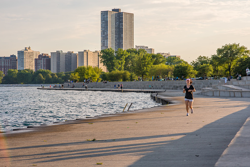 Chicago, IL, July 15, 2017: Woman jogs at the park area at Montrose Beach, with the Chicago skyline in the distance. Montrose Beach attracts many visitors for outdoor activities each summer.