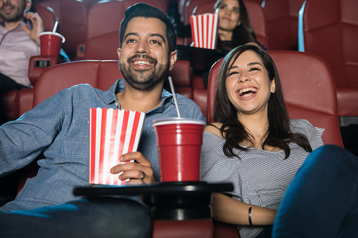 Latin couple laughing and having a good time while watching a comedy in the movie theater