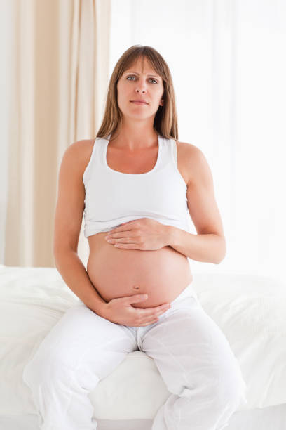 istock Cute pregnant female caressing her belly while sitting on a bed 824030060