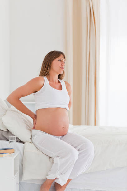 istock Charming pregnant female having a back pain while sitting on a bed 824030150