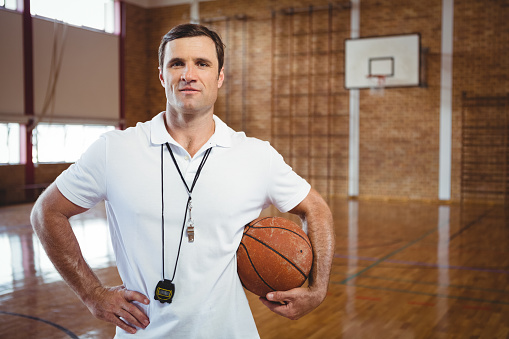 Portrait of confident basketball coach holding ball while standing in court