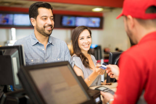 Woman paying for tickets on a date Portrait of a good looking Hispanic couple on a date at the movie theater while the woman pays for the tickets box office stock pictures, royalty-free photos & images