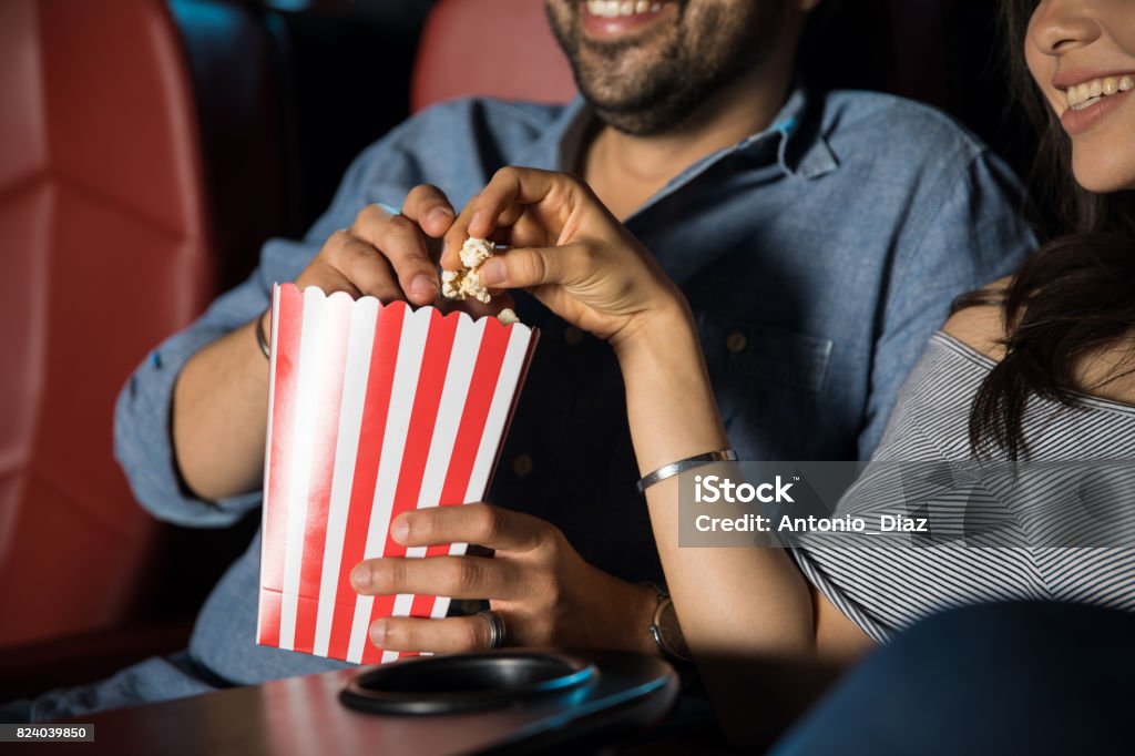 Eating popcorn at the movie theater Man touching the hand of his date while grabbing some popcorn at the movie theater Movie Theater Stock Photo