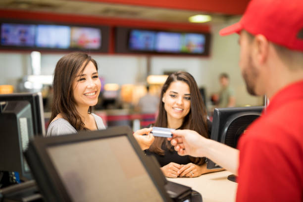 Female friends buying movie tickets Point of view of a male worker getting a credit card from a pair of friends at the movie theater box office photos stock pictures, royalty-free photos & images