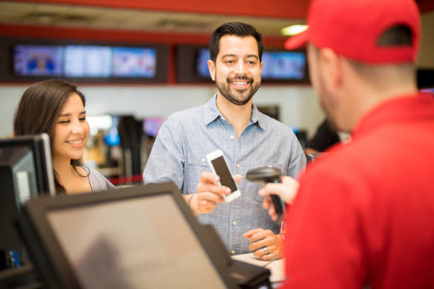 Using a barcode for tickets at the movies Attractive couple buying tickets at the movie theater and using a smartphone to show a barcode to an employee box office stock pictures, royalty-free photos & images