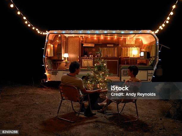 Man And Woman Sitting By Tree Next To Home Stock Photo - Download Image Now - Christmas, Camping, Motor Home