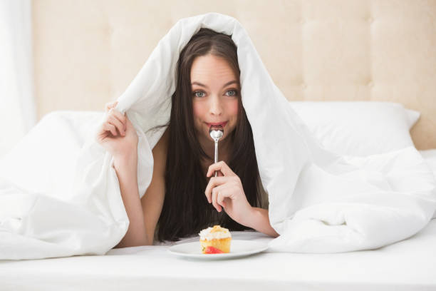 istock Pretty brunette eating cupcake in bed 824060196