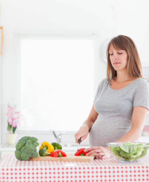 istock Pretty pregnant woman posing while cooking vegetables 824060968