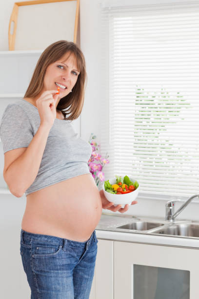 istock Lovely pregnant woman eating vegetables while standing 824063460