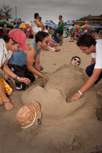 Montanita Mountaineer Ecuador Montañita Montanita, Santa Elena, Ecuador - February 4, 2012: A group of friends buries another in the sand, preparing to watch the sunset off the Ecuadorian coast. montanita ecuador stock pictures, royalty-free photos & images