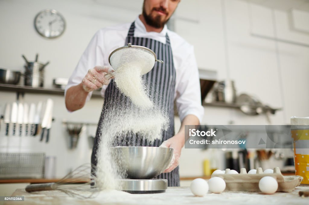 Pastry cook process Chef sifting flour through bolter into metallic bowl Confectioner Stock Photo