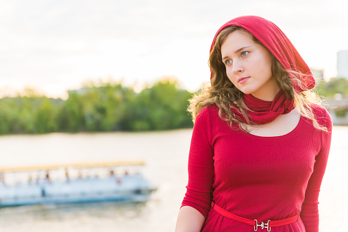 Young woman in red dress with scarf on head sitting thinking by Potomac River during sunset