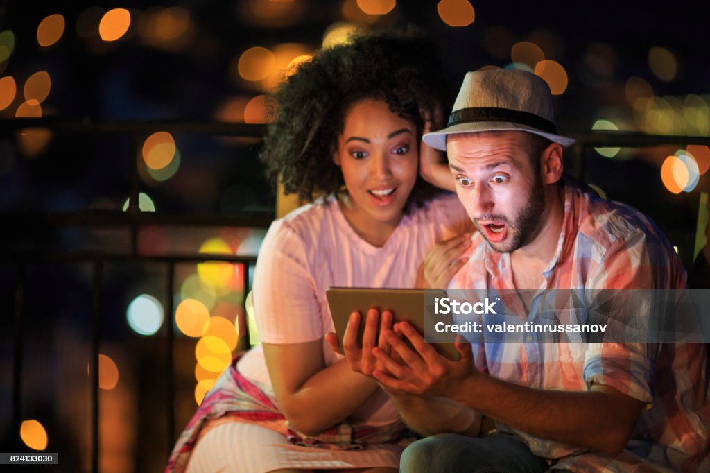 Couple having fun on street Couple having fun, using digital tablet on street, at night. Both with casual clothes. Surprise Stock Photo