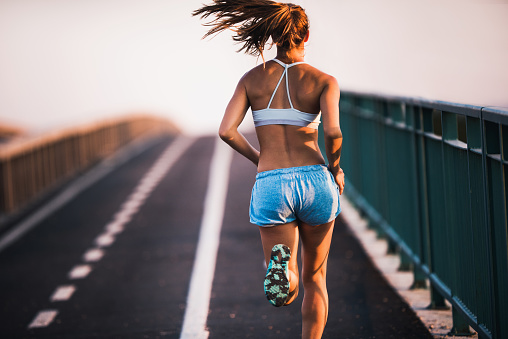 Back view of muscular build woman exercising outdoors and running on the street. Copy space.