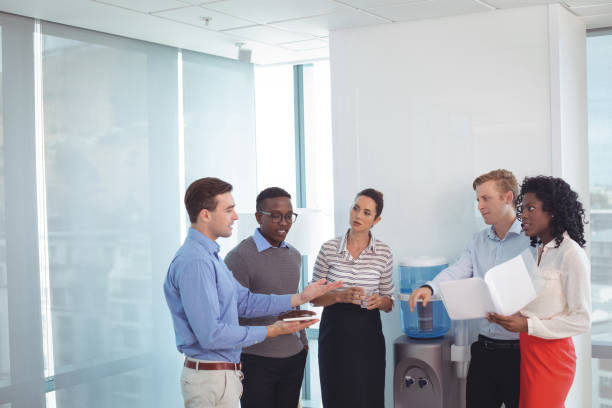 Young business partners discussing at office Young business partners discussing while standing at office cooler stock pictures, royalty-free photos & images