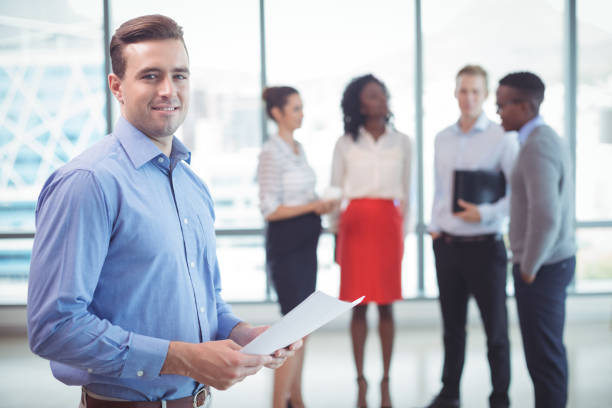 istock Smiling businessman holding documets with colleagues standing in background 824178370