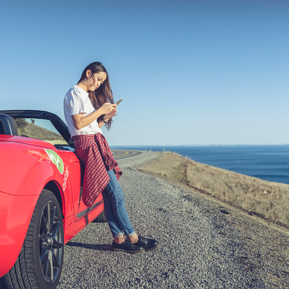 woman standing by her car and looking at smartphone at a sunny day,san juan island,usa.