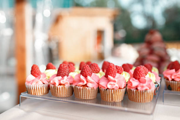 istock candy bar. many mini vanilla cupcakes with flavoured buttercream decorated with fresh raspberries in a line on table. 824234912