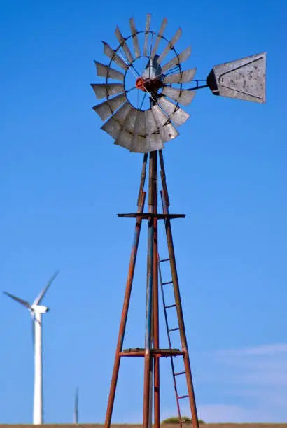 Old iron windmill for pumping drinking water for livestock on the Wyoming plains with wind generators in the background.