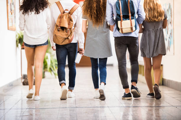 Unrecognizable teenage students in high school hall. Group attractive teenage students in high school hall. Rear view. female high school student stock pictures, royalty-free photos & images