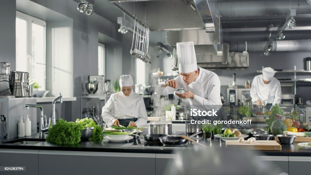 Berühmten Koch arbeitet in einer großen Küche mit seiner Hilfe. Küche ist voller Essen, Gemüse und Kochen Gerichte. Er versucht Geschmack. - Lizenzfrei Kochberuf Stock-Foto