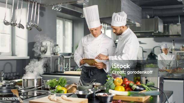 Dos Chefs Famosos Discutan Su Vídeo Blog Mientras Uso De Tablet Pc Trabajan En Una Cocina Profesional Grande Restaurante De Acero Inoxidable Foto de stock y más banco de imágenes de Chef