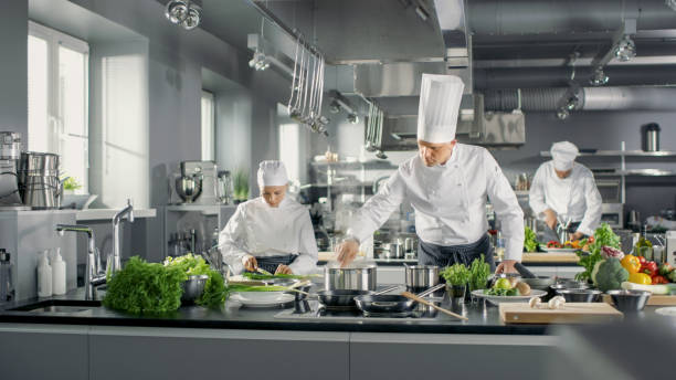 Famous Chef Works in a Big Restaurant Kitchen with His Help. Kitchen is Full of Food, Vegetables and Boiling Dishes. Famous Chef Works in a Big Restaurant Kitchen with His Help. Kitchen is Full of Food, Vegetables and Boiling Dishes. buffet hotel people women stock pictures, royalty-free photos & images