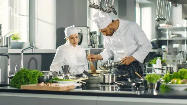 Photo of Famous Chef and His Female Apprentice Prepare Special Dish in a Modern Five Star Restaurant's Kitchen.