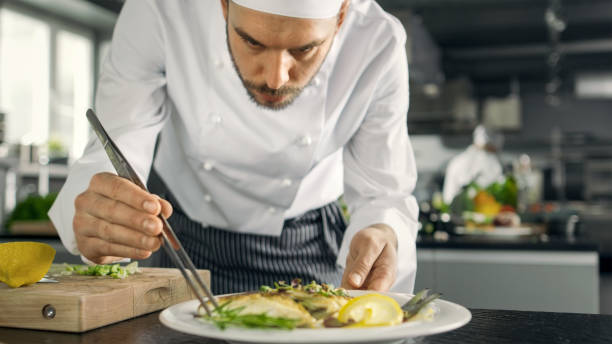 istock Famous Chef Decorates His Special Fish Dish with Some Greens. He Works in a Modern Kitchen. 824283976