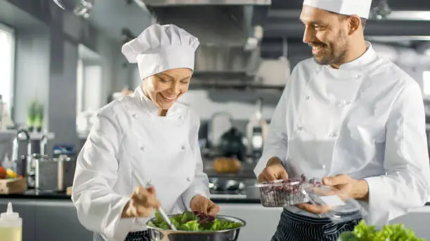 Photo of Male and Female Famous Chefs Team Prepare Salad for Their Five Star Restaurant. They Work on a Big Restaurant Stainless Steel Professional Kitchen.
