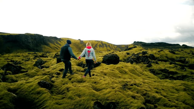 Aerial view of couple walking through the lava fields in iceland. Man and woman sit on the rock, enjoying the landscape