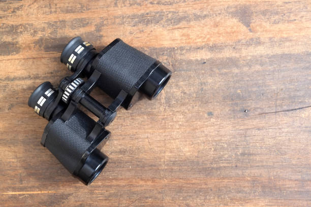 istock Old prism black color binoculars over wooden background closeup 824323854