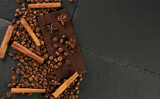 Aromatic set of chocolate bar, arabica coffee beans, anise and cinnamon on dark stone background with copy space