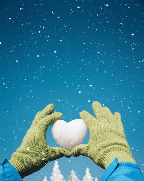 I love winter concept: hands holding a heart shape snowball in the air.