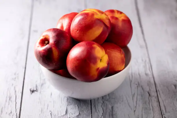 Nectarines sitting in a bowl that is sitting on wooden slats