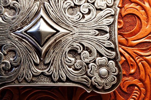 A silver belt buckle sits on top of a tooled leather surface.