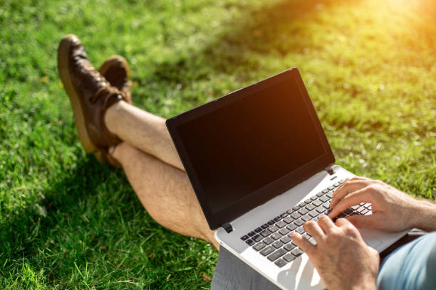 istock Cropped shot of man using laptop with blank screen while sitting on green grass 824370250