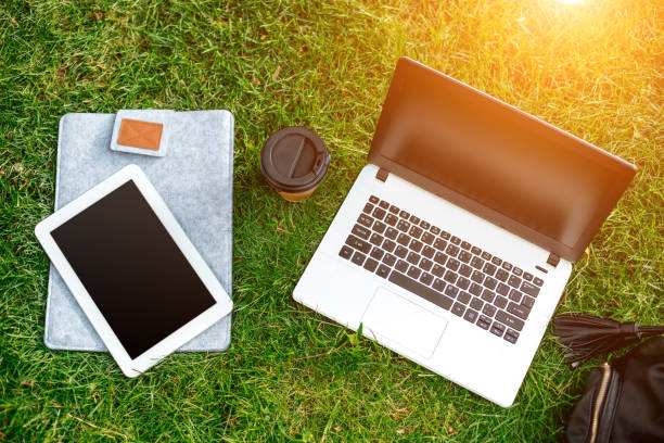 istock Laptop computer on green grass with coffee cup, bag and tablet in outdoor park 824378712