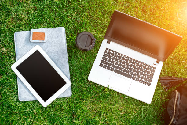 istock Laptop computer on green grass with coffee cup, bag and tablet in outdoor park 824383110