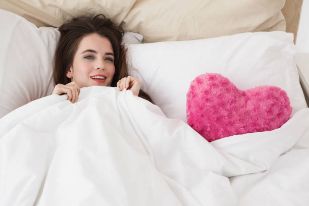 istock Pretty brunette in bed with heart cushion 824570348