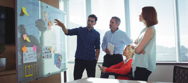 Young businessman discussing with colleagues at office Young businessman discussing with colleagues over whiteboard at office sales executive stock pictures, royalty-free photos & images