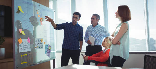 Young businessman discussing with colleagues at office Young businessman discussing with colleagues over whiteboard at office whiteboard stock pictures, royalty-free photos & images