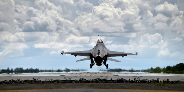 Jet fighter landing and taking off from runway in a hot day with cloudy sky in background