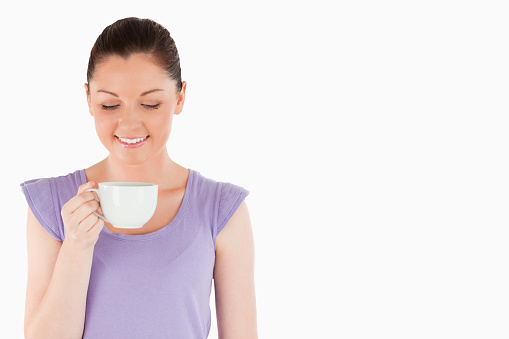 Lovely woman enjoying a cup of coffee while standing against a white background